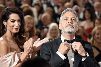 George Clooney richtet seine Fliege, seine Frau Amal applaudiert.