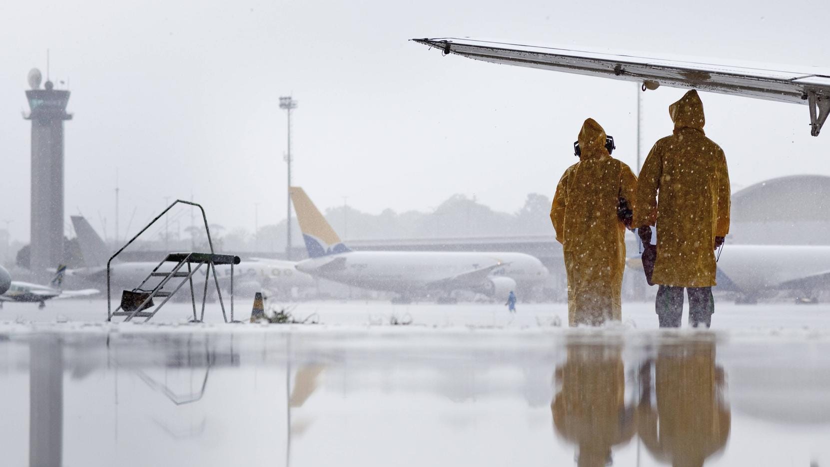 Mitarbeiter des Flughafen Manaus suchen während eines Regenschauers Schutz unter der Tragflaeche eines Flugzeuges: Der Flugverkehr im Sommer wird besonders durch Unwetter und Streiks beeinträchtigt.