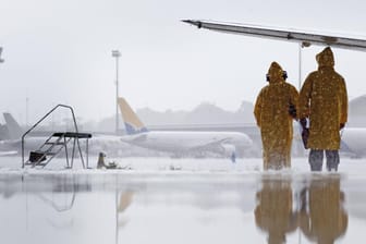 Mitarbeiter des Flughafen Manaus suchen während eines Regenschauers Schutz unter der Tragflaeche eines Flugzeuges: Der Flugverkehr im Sommer wird besonders durch Unwetter und Streiks beeinträchtigt.