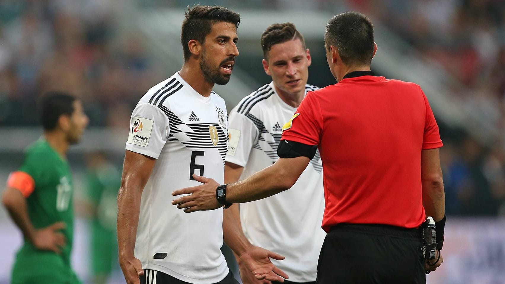 Sami Khedira (l.) und Julian Draxler (m.) fragen im Testspiel gegen Saudi-Arabien bei Schiedsrichter Slavko Vincic nach.