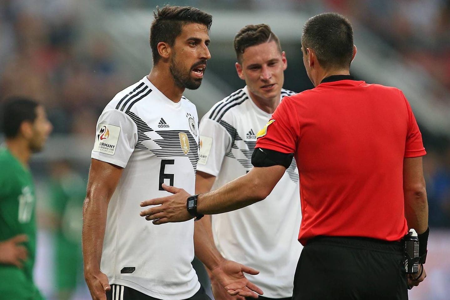 Sami Khedira (l.) und Julian Draxler (m.) fragen im Testspiel gegen Saudi-Arabien bei Schiedsrichter Slavko Vincic nach.