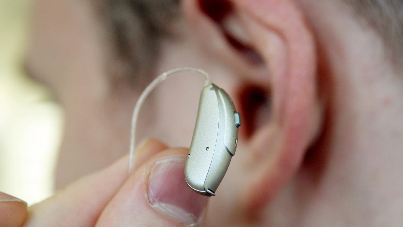 Ein Mitarbeiter hält bei einem Hörgeräteakustiker zur Demonstration ein Hörgerät vor sein Ohr.