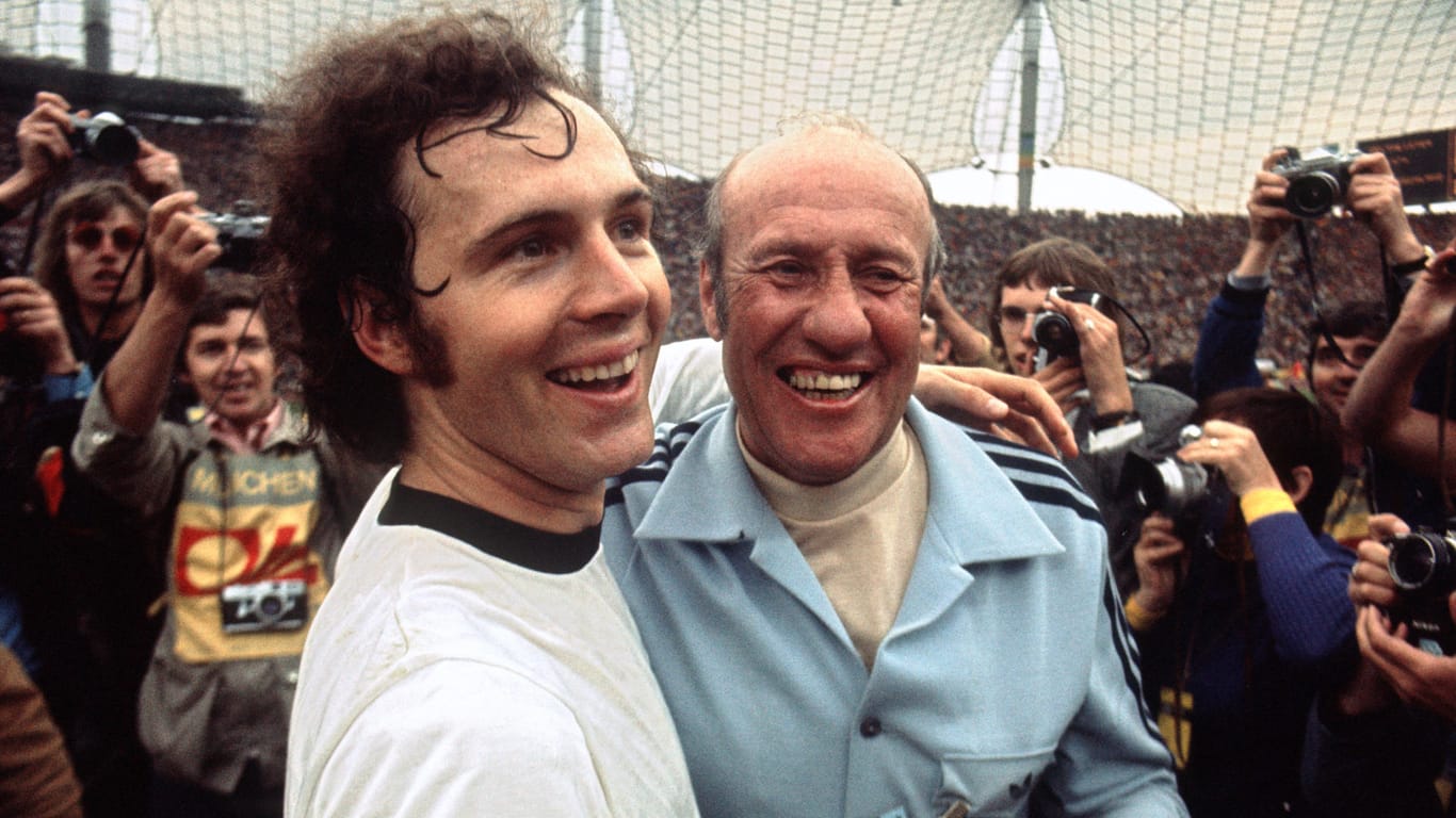 Überglücklich jubelnd liegen sich Franz Beckenbauer (links) und Trainer Helmut Schön nach dem 2:1-Sieg über die Niederlande im Endspiel der Fußball-Weltmeisterschaft am 07.07.1974 im Münchner Olympiastadion in den Armen.