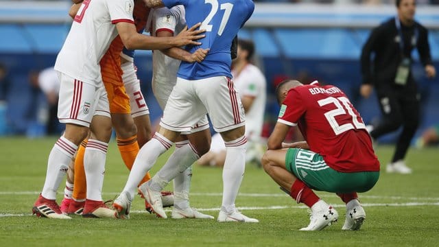 Der Marokkaner Aziz Bouhaddouz (r) hockt nach seinem Eigentor auf dem Rasen, während die Spieler des Iran den Sieg bejubeln. Der Marokkaner Aziz Bouhaddouz (r) hockt nach seinem Eigentor auf dem Rasen, während die Spieler des Iran den Sieg bejubeln.