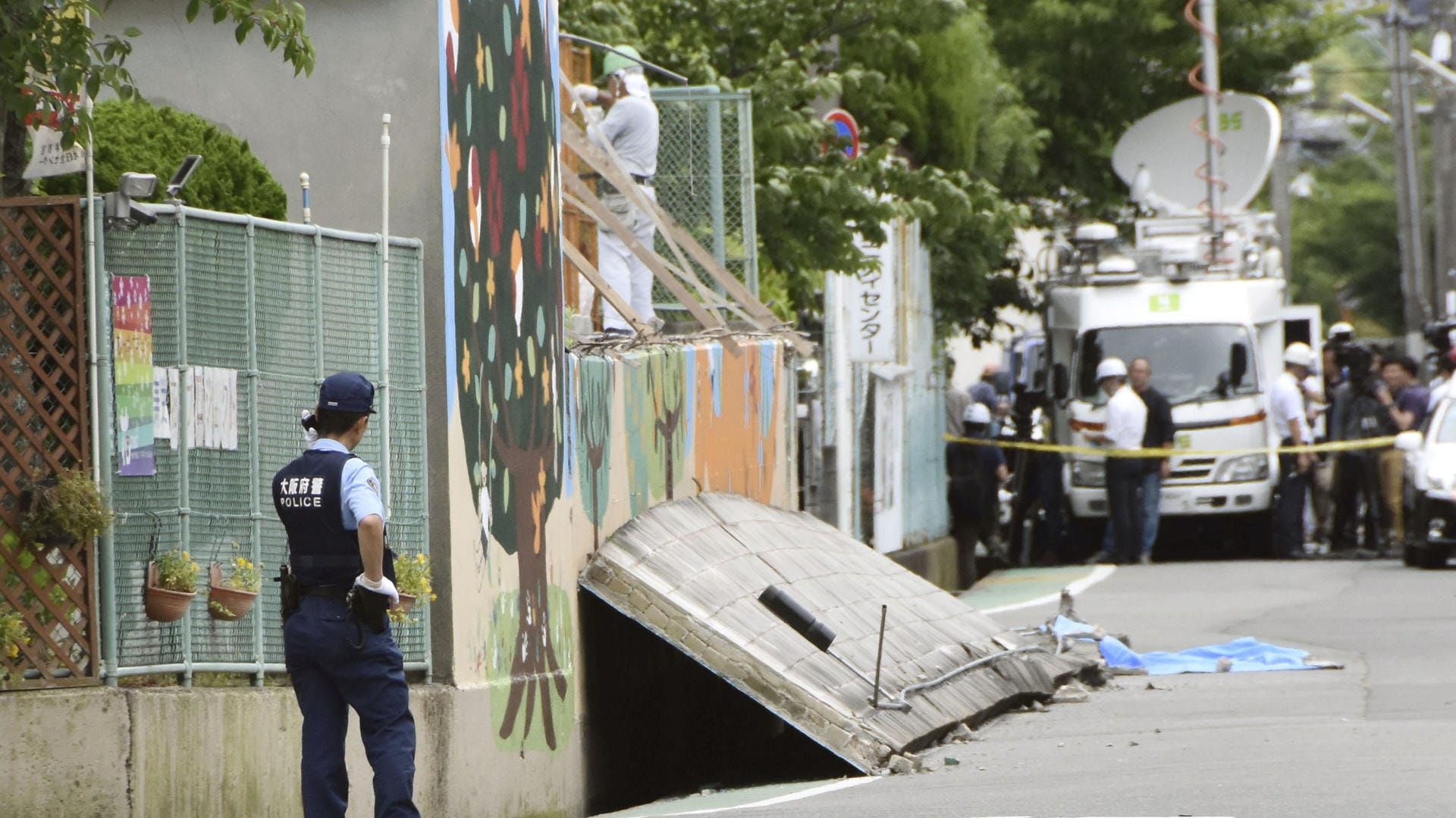 Ein Polizist hält vor einer Schule in Takatsuki in der Provinz Osaka Wache: Ein Mädchen wurde von der Wand eines Swimmingpools, die bei dem Erdbeben einstürzte, erschlagen. Ein Polizist hält vor einer Schule in Takatsuki in der Provinz Osaka Wache: Ein Mädchen wurde von der Wand eines Swimmingpools, die bei dem Erdbeben einstürzte, erschlagen.