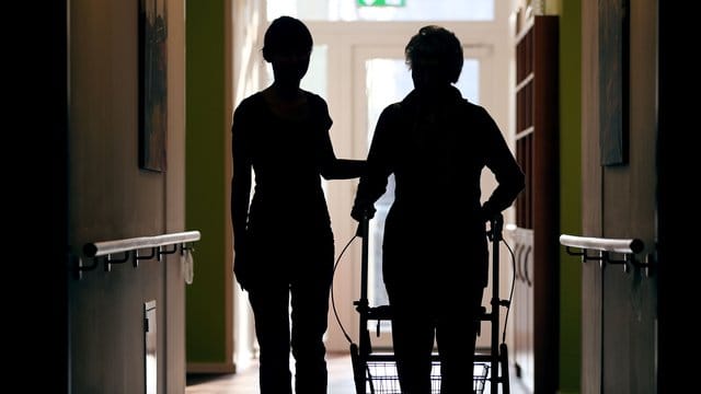 Eine Pflegekraft begleitet eine alte Frau beim Gang über den Flur.