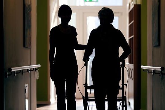 Eine Pflegekraft begleitet eine alte Frau beim Gang über den Flur.