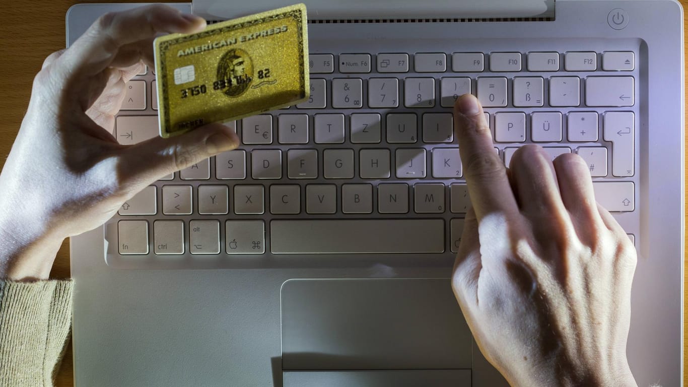 Ein Mann tippt am Computer mit Kreditkarte in der Hand: Betrüger geben sich als Microsoft-Mitarbeiter aus und versuchen, an Geld und Daten von Nutzern zu kommen.