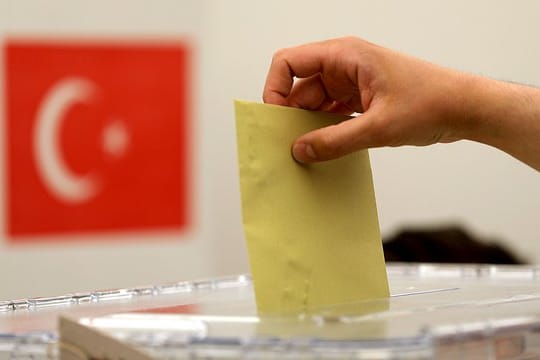 Ein Stimmzettel wird in eine Urne geworfen.