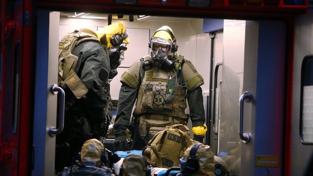 SEK-Beamten mit Atemschutzmasken und Schutzanzügen stehen in einem Fahrzeug vor einem Wohnkomplex. SEK-Beamten mit Atemschutzmasken und Schutzanzügen stehen in einem Fahrzeug vor einem Wohnkomplex.