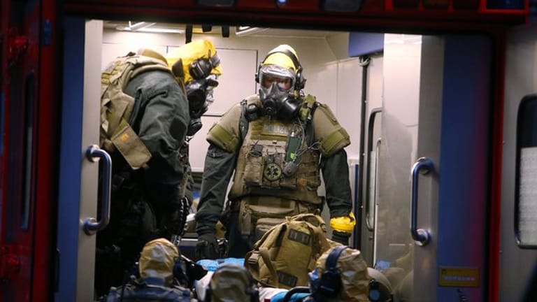SEK-Beamten mit Atemschutzmasken und Schutzanzügen stehen in einem Fahrzeug vor einem Wohnkomplex.