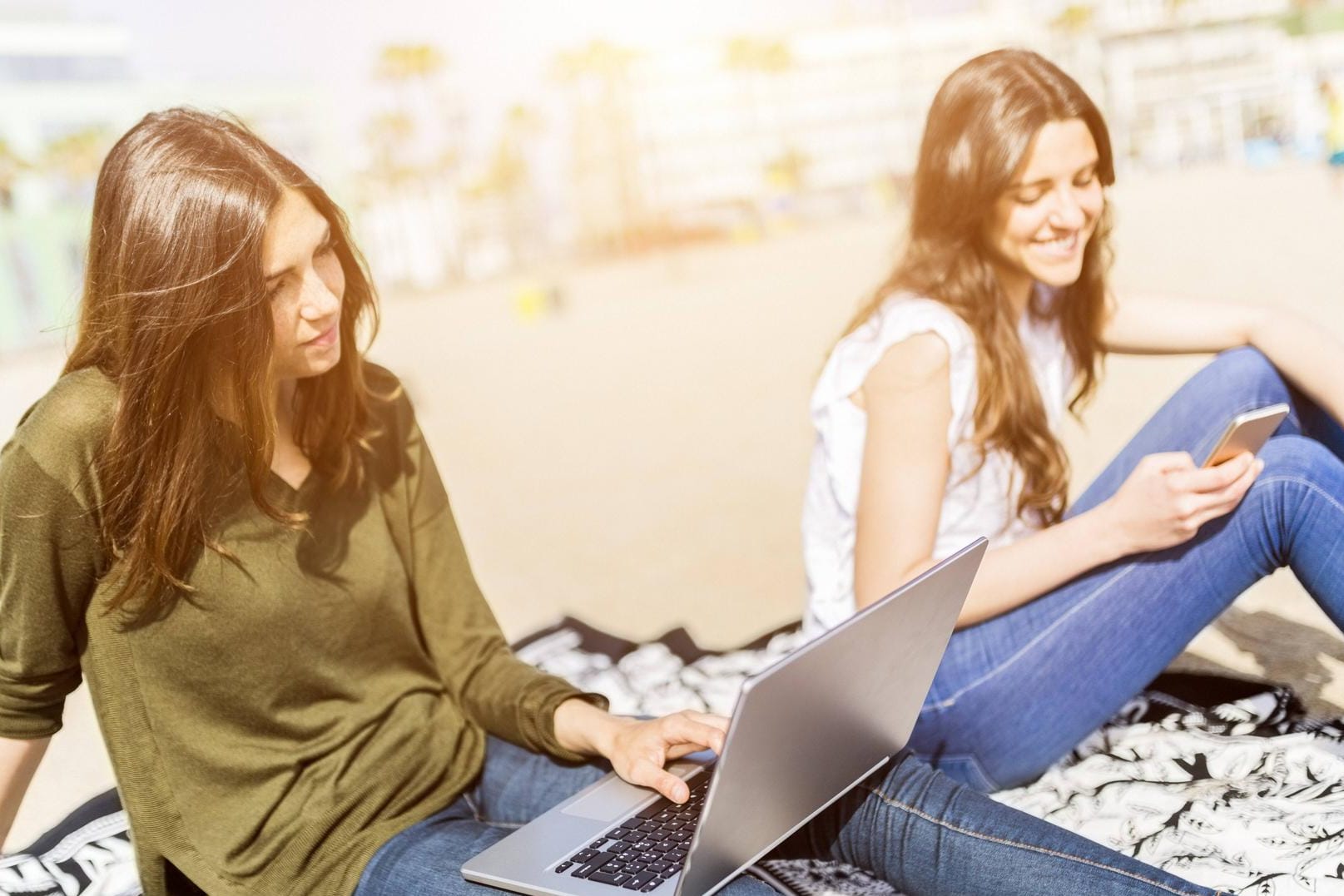 Zwei junge Frauen sitzen mit Laptop und Smartphone am Strand: Nur wenige Urlauber verzichten in den Ferien auf ihre Elektronik.