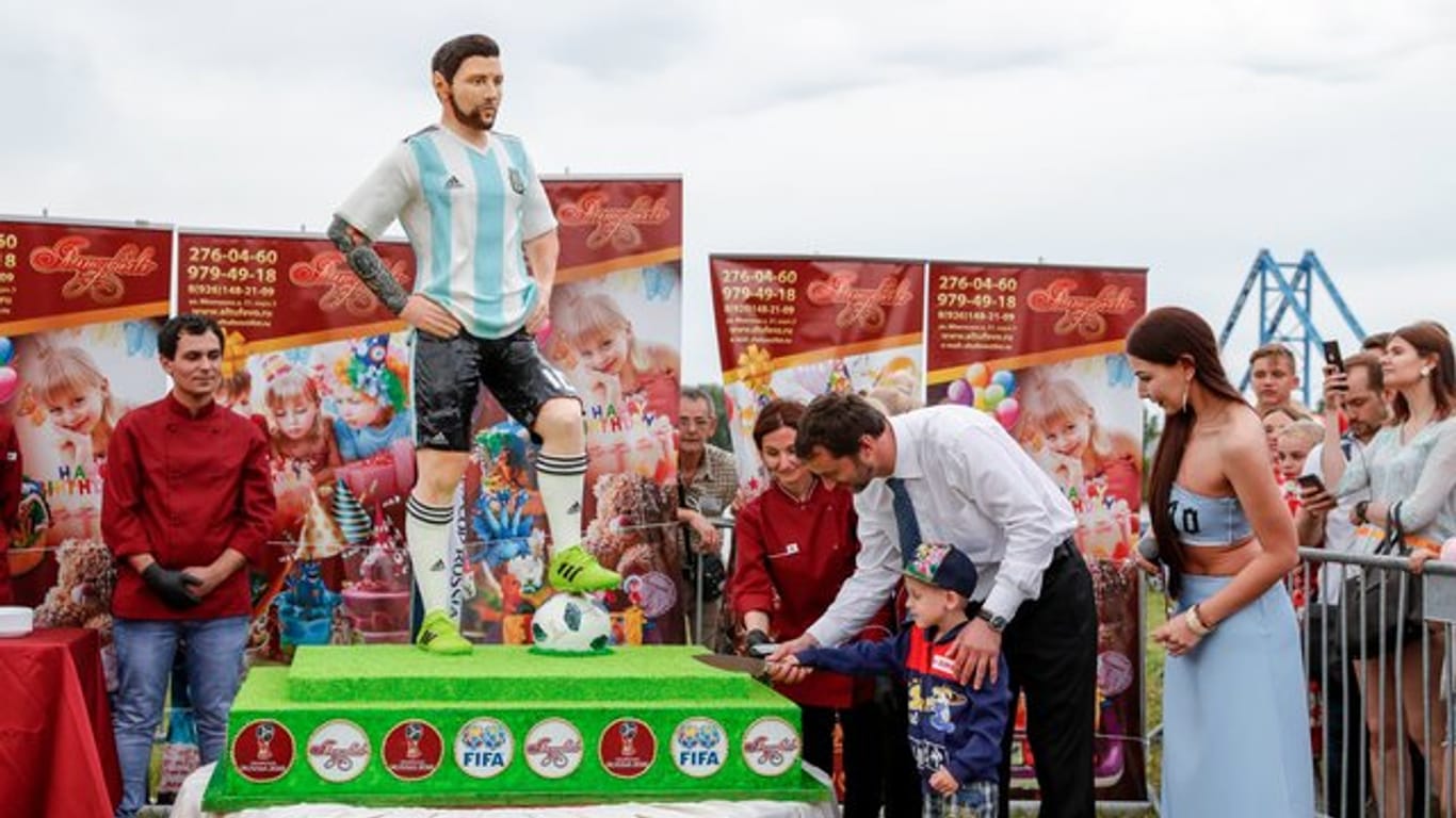 Der Bürgermeister der Stadt Bronnizy hilft einem Jungen die Geburtstagstorte von Argentiniens Nationalspieler Lionel Messi anzuschneiden.