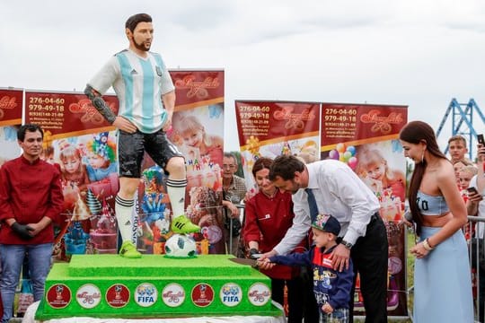 Der Bürgermeister der Stadt Bronnizy hilft einem Jungen die Geburtstagstorte von Argentiniens Nationalspieler Lionel Messi anzuschneiden.
