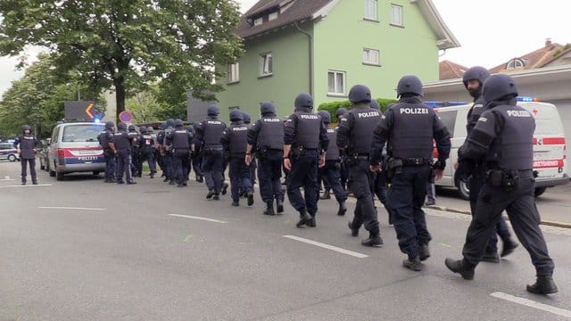 Polizisten mit Helmen und schusssicheren Westen gehen über eine Straße in der Nähe des Tatorts in Bregenz.