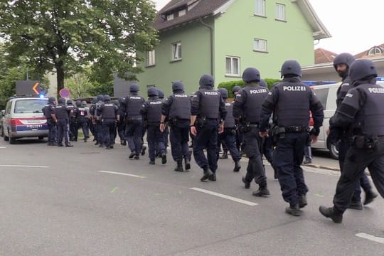 Polizisten mit Helmen und schusssicheren Westen gehen über eine Straße in der Nähe des Tatorts in Bregenz.