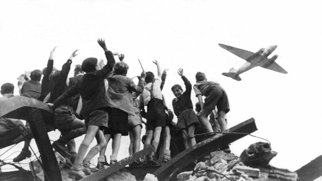 West-Berliner Jungen stehen 1948 auf einem Trümmerberg und winken einem sogenannten Rosinenbomber zu. West-Berliner Jungen stehen 1948 auf einem Trümmerberg und winken einem sogenannten Rosinenbomber zu.