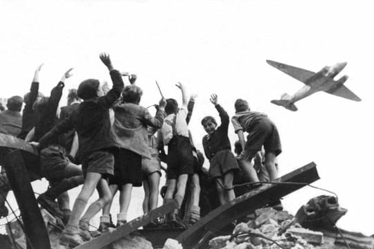 West-Berliner Jungen stehen 1948 auf einem Trümmerberg und winken einem sogenannten Rosinenbomber zu.