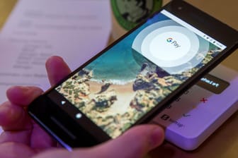 Google Pay: Ein Gast demonstriert mit einem Smartphone und der App des neuen Bezahldienstes in einem Café das Bezahlen mit dem Handy.