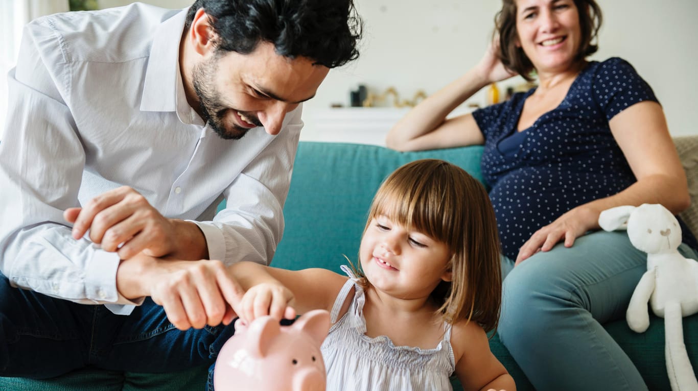 Eine Familie wirft Geld in ein Sparschwein: Die Bundesregierung plant, das Kindergeld um zehn Euro im Monat pro Kind zu erhöhen.