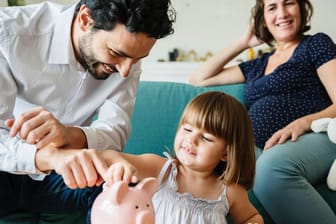 Eine Familie wirft Geld in ein Sparschwein: Die Bundesregierung plant, das Kindergeld um zehn Euro im Monat pro Kind zu erhöhen.
