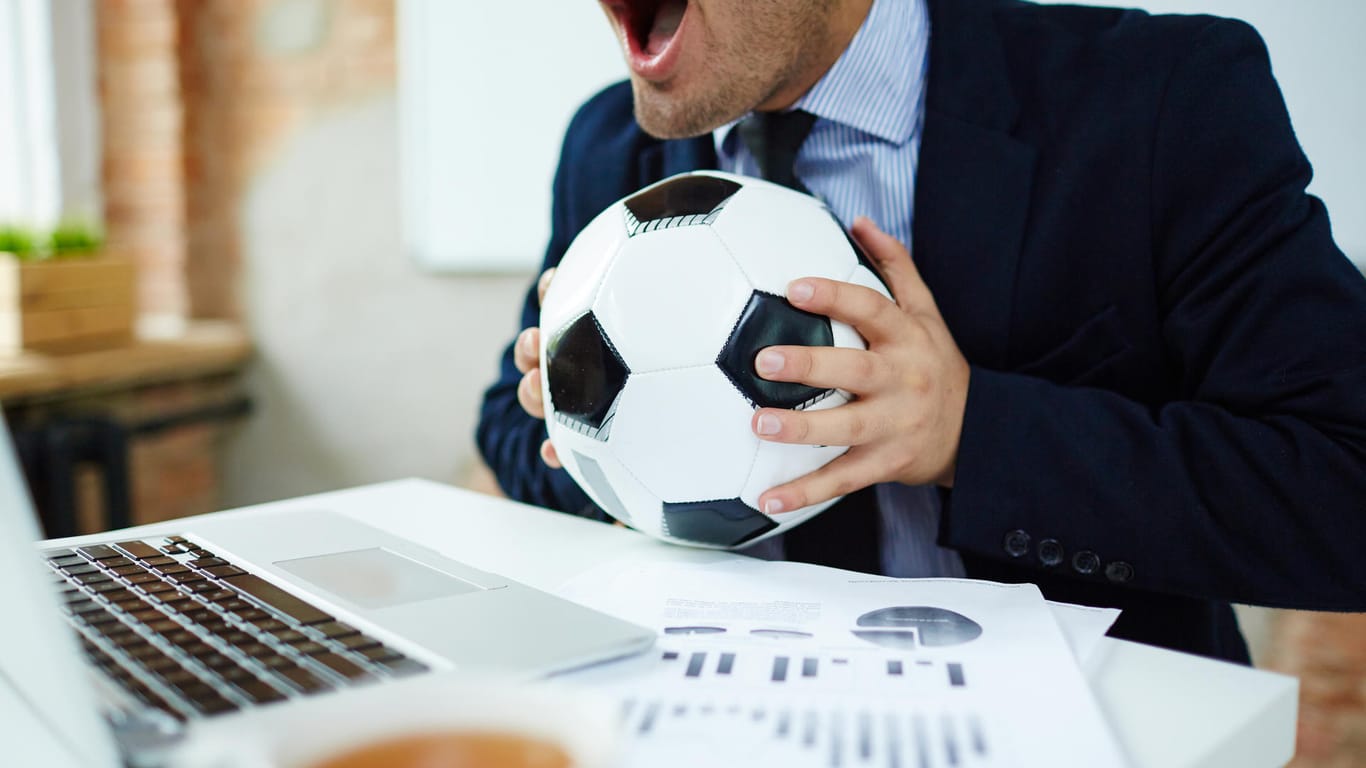 Mann mit Fußball am Arbeitsplatz: Sie dürfen die WM-Spiele bei der Arbeit nur verfolgen, wenn der Arbeitgeber es ausdrücklich gestattet.
