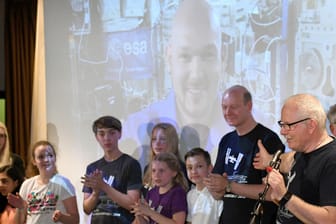 Schüler stehen in der Aula des Werner Heisenberg Gymnasiums in Leverkusen: Sie konnten Fragen an den deutschen Astronauten Alexander Gerst (Hintergrund) richten.