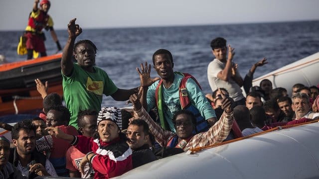 Migranten in einem Schlauchboot winken vor der Küste Libyens zu einem Mitglied der Hilfsorganisation Proactiva Open Arms.