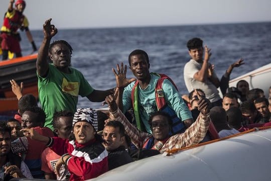 Migranten in einem Schlauchboot winken vor der Küste Libyens zu einem Mitglied der Hilfsorganisation Proactiva Open Arms.