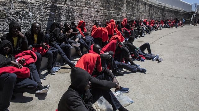 Migranten sitzen nach ihrer Rettung in der Straße von Gibraltar im Hafen von Tarifa in Spanien in Decken gehüllt an einer Mauer. Migranten sitzen nach ihrer Rettung in der Straße von Gibraltar im Hafen von Tarifa in Spanien in Decken gehüllt an einer Mauer.