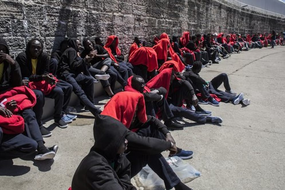 Migranten sitzen nach ihrer Rettung in der Straße von Gibraltar im Hafen von Tarifa in Spanien in Decken gehüllt an einer Mauer.