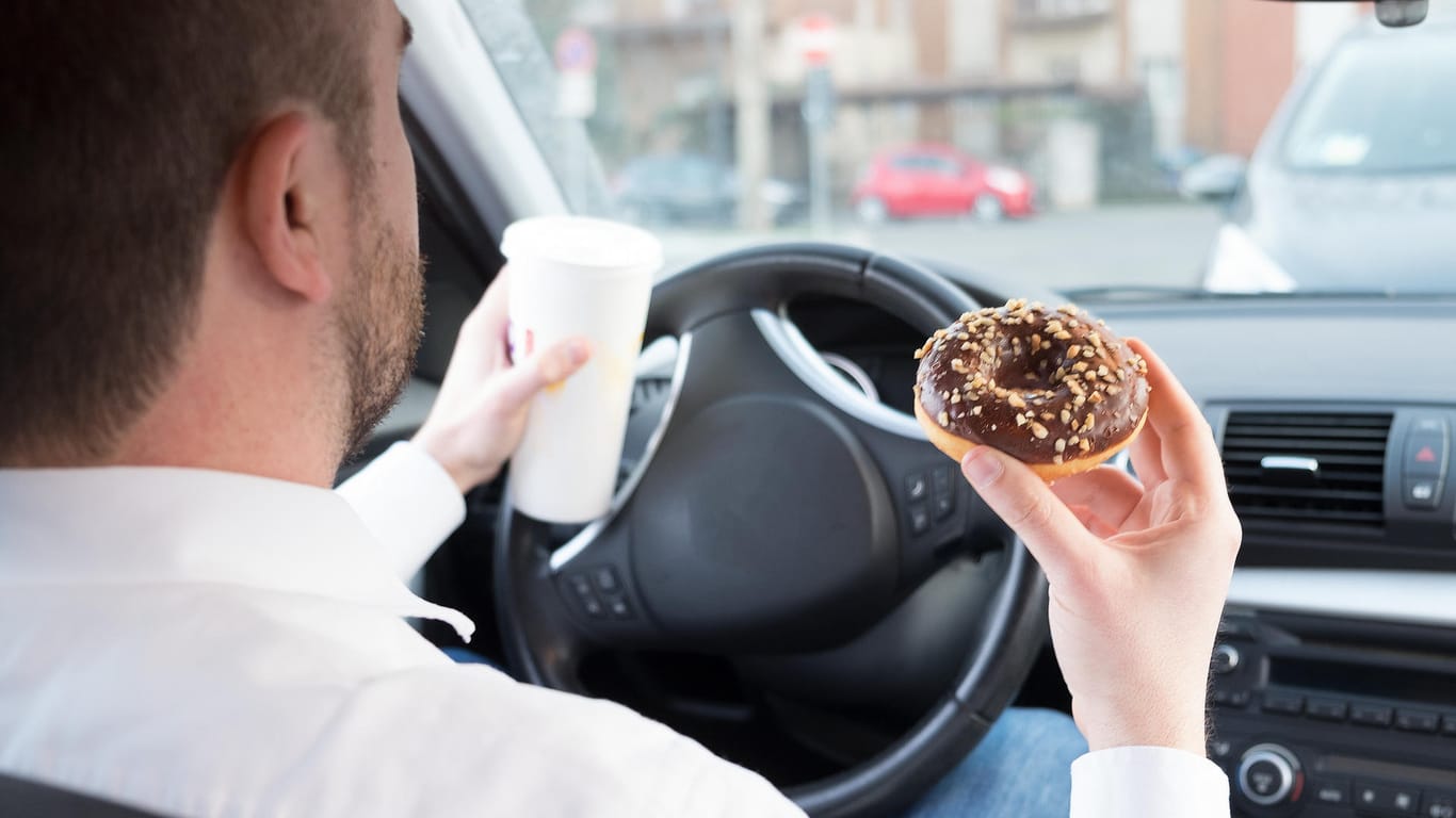 Mann im Auto isst einen Schokoladen-Donut