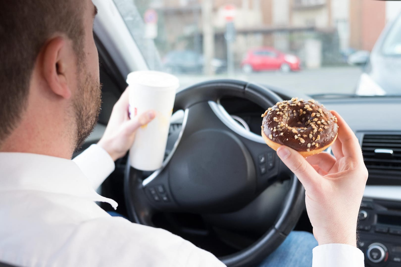 Mann im Auto isst einen Schokoladen-Donut