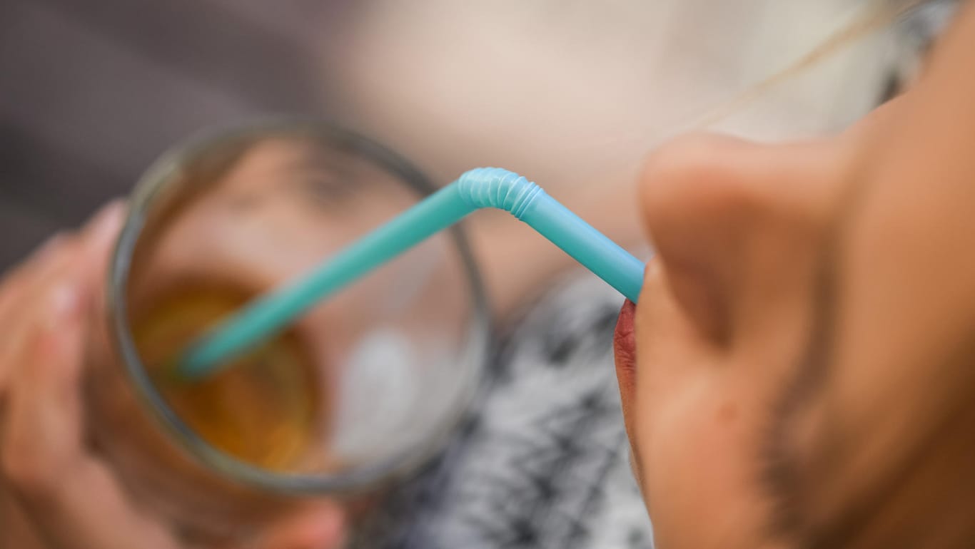 Ein Mädchen trinkt mit einem Strohhalm aus Plastik aus einem Glas.