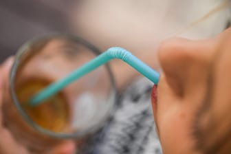 Ein Mädchen trinkt mit einem Strohhalm aus Plastik aus einem Glas.