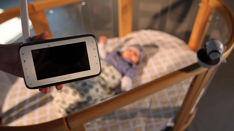 Eine Frau hält ein Video-Babyfon über ein Kinderbett: Mitten in der Nacht hat eine Mutter einen Unbekannten im Kinderzimmer aufgefunden. Das Babyfon alarmierte sie.