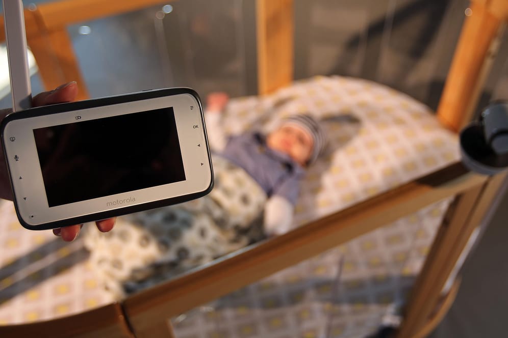 Eine Frau hält ein Video-Babyfon über ein Kinderbett: Mitten in der Nacht hat eine Mutter einen Unbekannten im Kinderzimmer aufgefunden. Das Babyfon alarmierte sie.