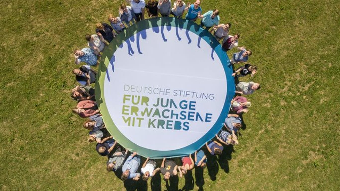 Teilnehmer einer Veranstaltung der Deutschen Stiftung für junge Erwachsene mit Krebs rund um das Logo der Organisation.