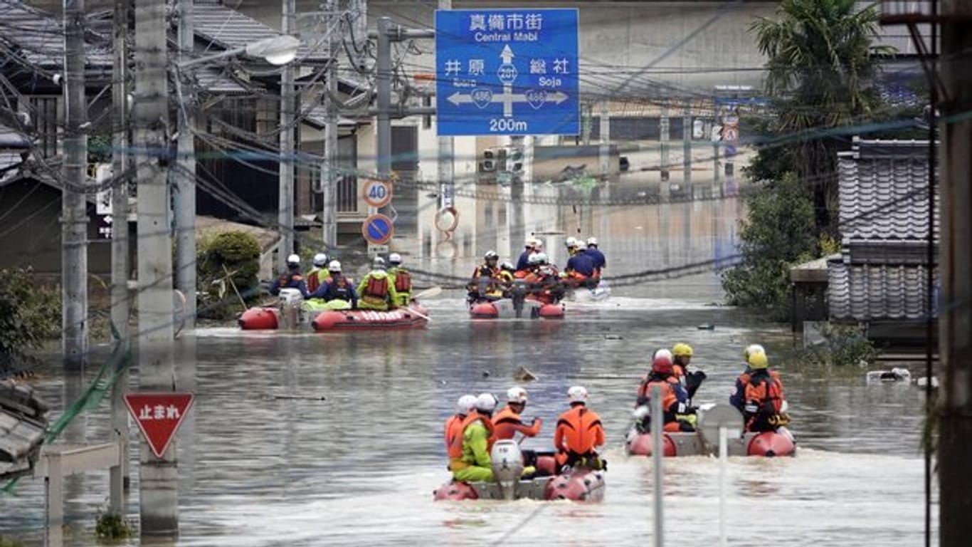 Rettungsmannschafen fahren in Kurashiki mit Booten über eine überflutet Straße.