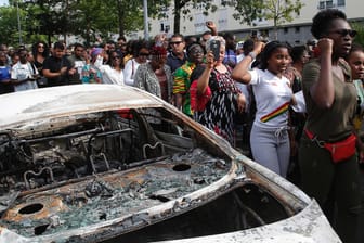 Demonstranten ziehen an einem ausgebrannten Auto vorbei: Am Dienstag war ein 22-Jähriger durch den Schuss eines Polizisten getötet worden.
