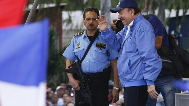 In Begleitung eines bewaffneten Leibwächters winkt Nicaraguas Präsident Daniel Ortega getreuen Parteianhängern zu. In Begleitung eines bewaffneten Leibwächters winkt Nicaraguas Präsident Daniel Ortega getreuen Parteianhängern zu.
