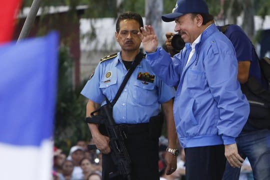 In Begleitung eines bewaffneten Leibwächters winkt Nicaraguas Präsident Daniel Ortega getreuen Parteianhängern zu.