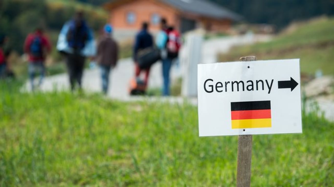 Flüchtlinge gehen nahe der deutschen Grenze hinter einem Schild mit der Aufschrift "Germany".