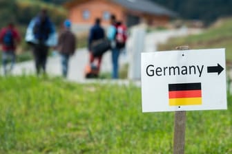 Flüchtlinge gehen nahe der deutschen Grenze hinter einem Schild mit der Aufschrift "Germany".