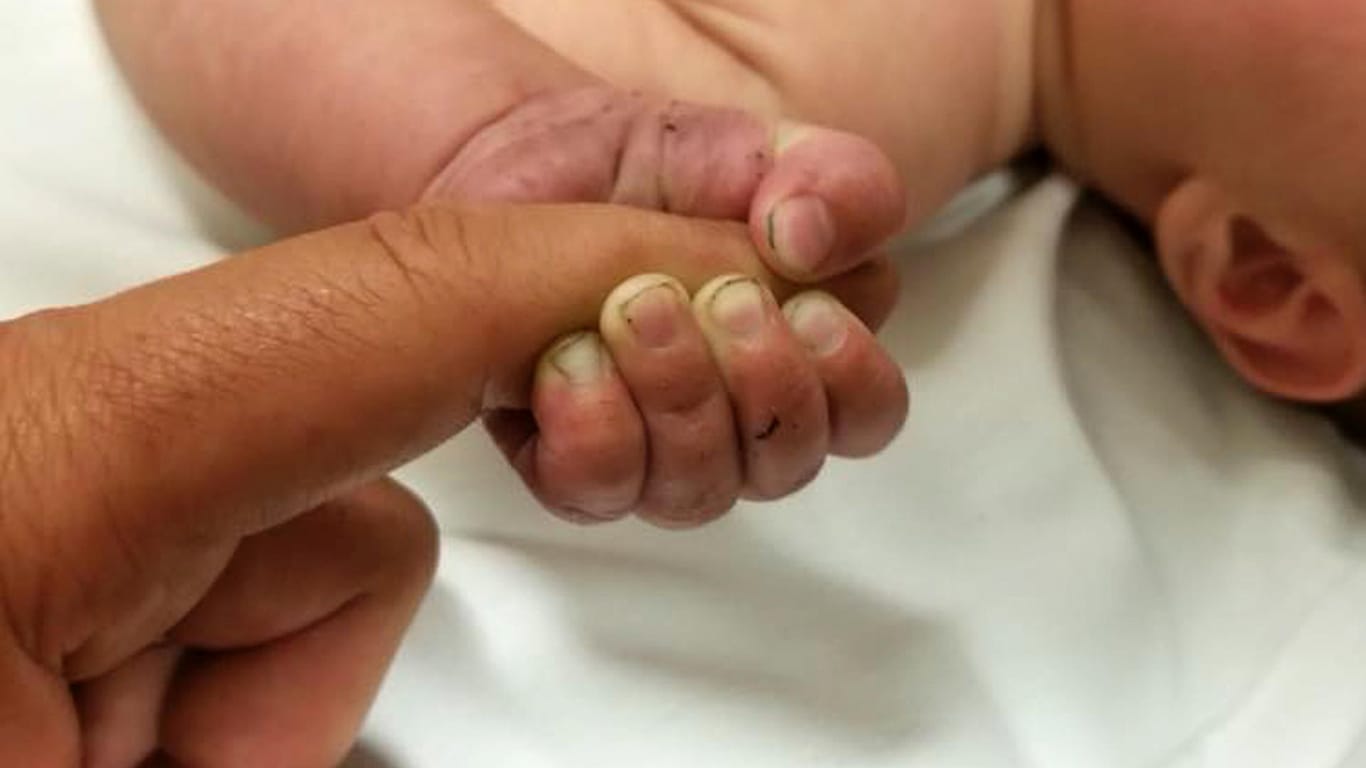 Die Hand eines fünf Monate altes Baby umfasst einen Finger: Das "schwache Wimmern" des Kindes machte einen Polizisten schließlich auf den Säugling aufmerksam.