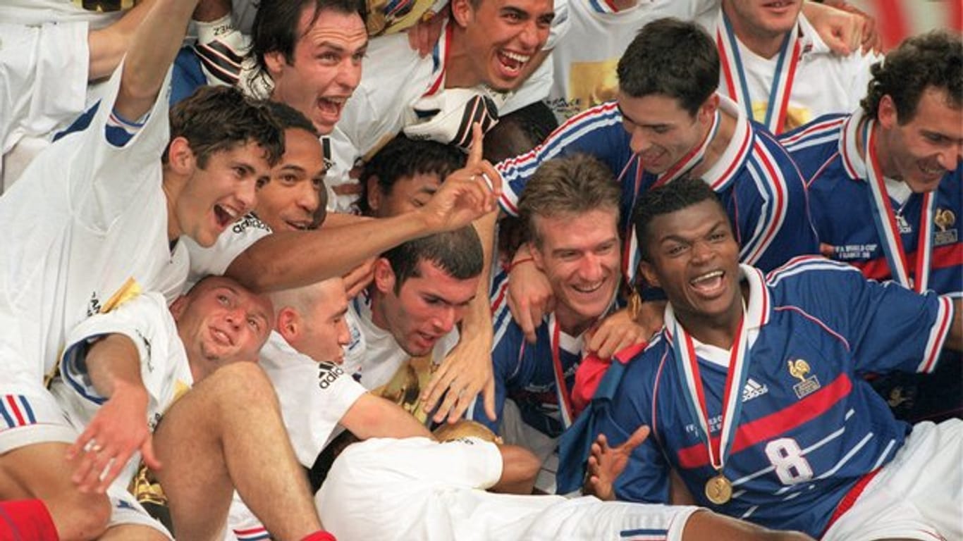 Die französischen Spieler um ihren Kapitän Didier Deschamps (M/lachend) und den zweifachen Finaltorschützen Zinedine Zidane (links daneben) jubeln mit dem WM-Weltpokal.