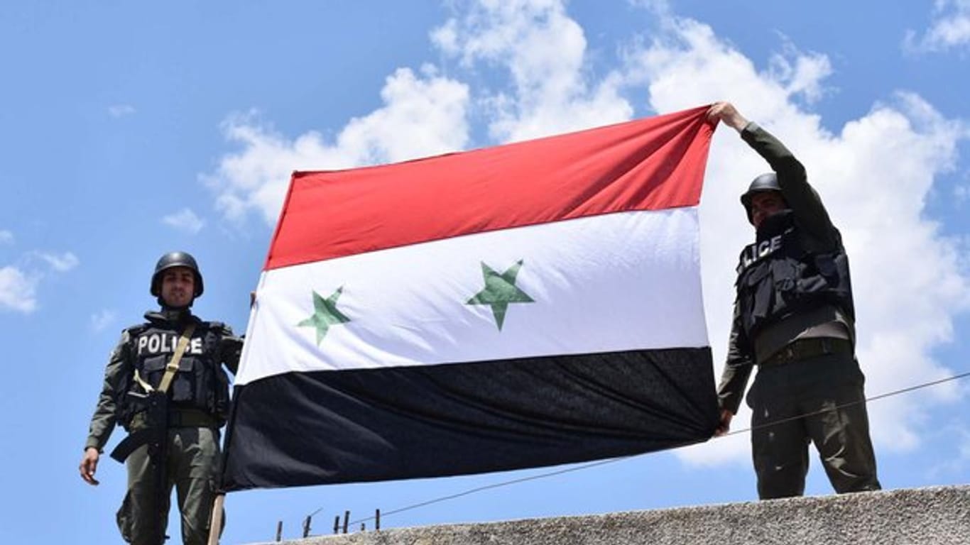 Syrische Polizisten halten eine syrische Flagge hoch.