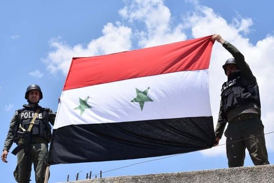 Syrische Polizisten halten eine syrische Flagge hoch.