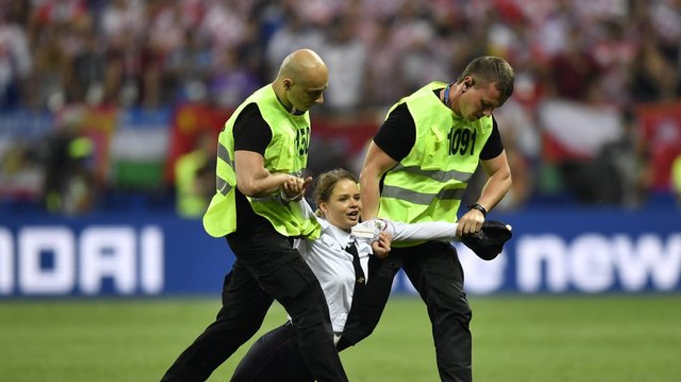 Zwei Sicherheitsmänner ziehen eine Frau in Uniform, die im Luschnikistadion aufs Spielfeld gelaufen war, vom Rasen.