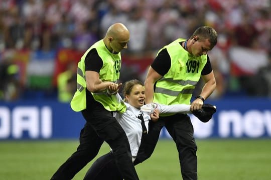 Zwei Sicherheitsmänner ziehen eine Frau in Uniform, die im Luschnikistadion aufs Spielfeld gelaufen war, vom Rasen.